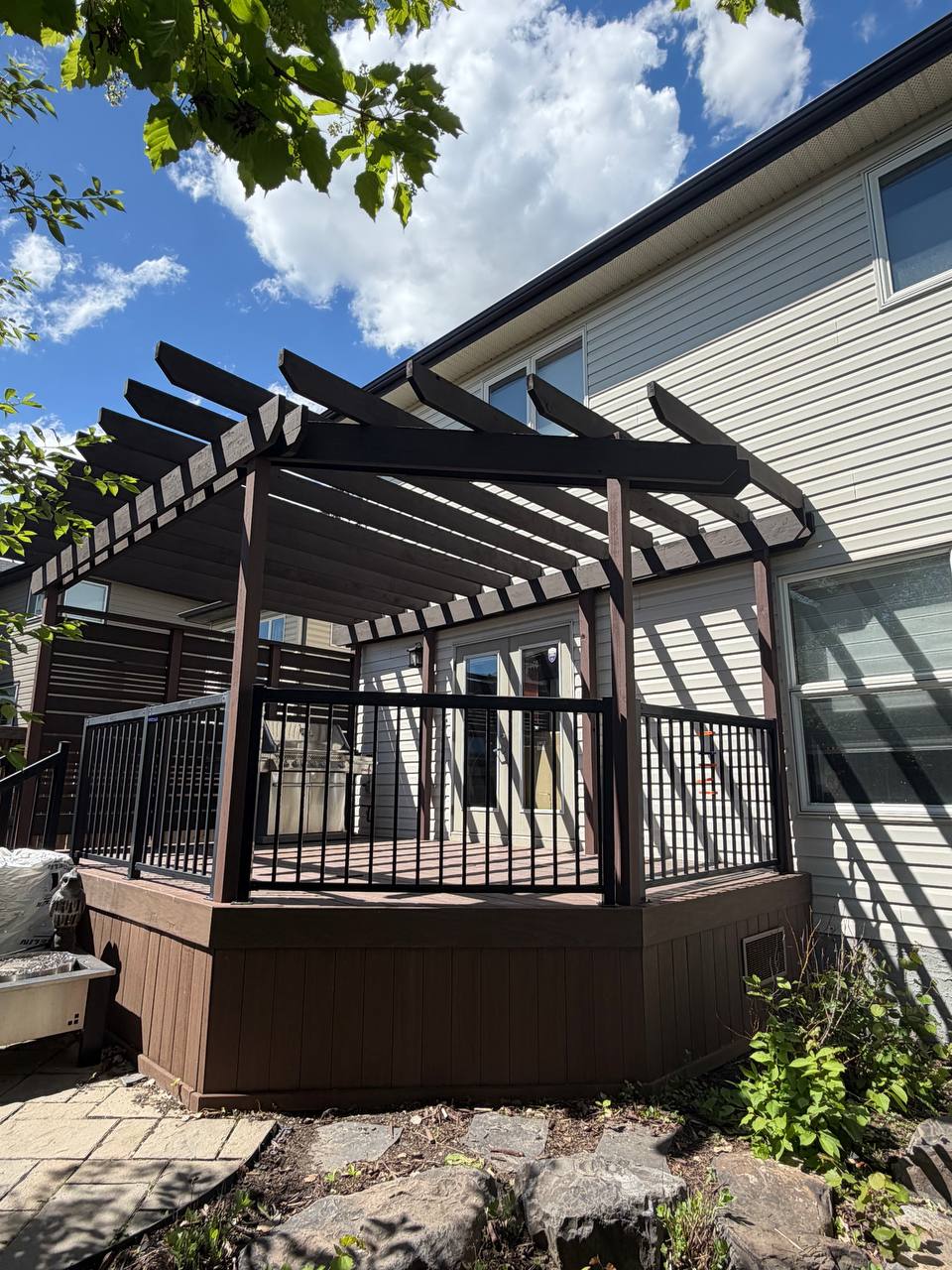 Calgary deck restaining project with pergola beams and black railing by Fix On Call