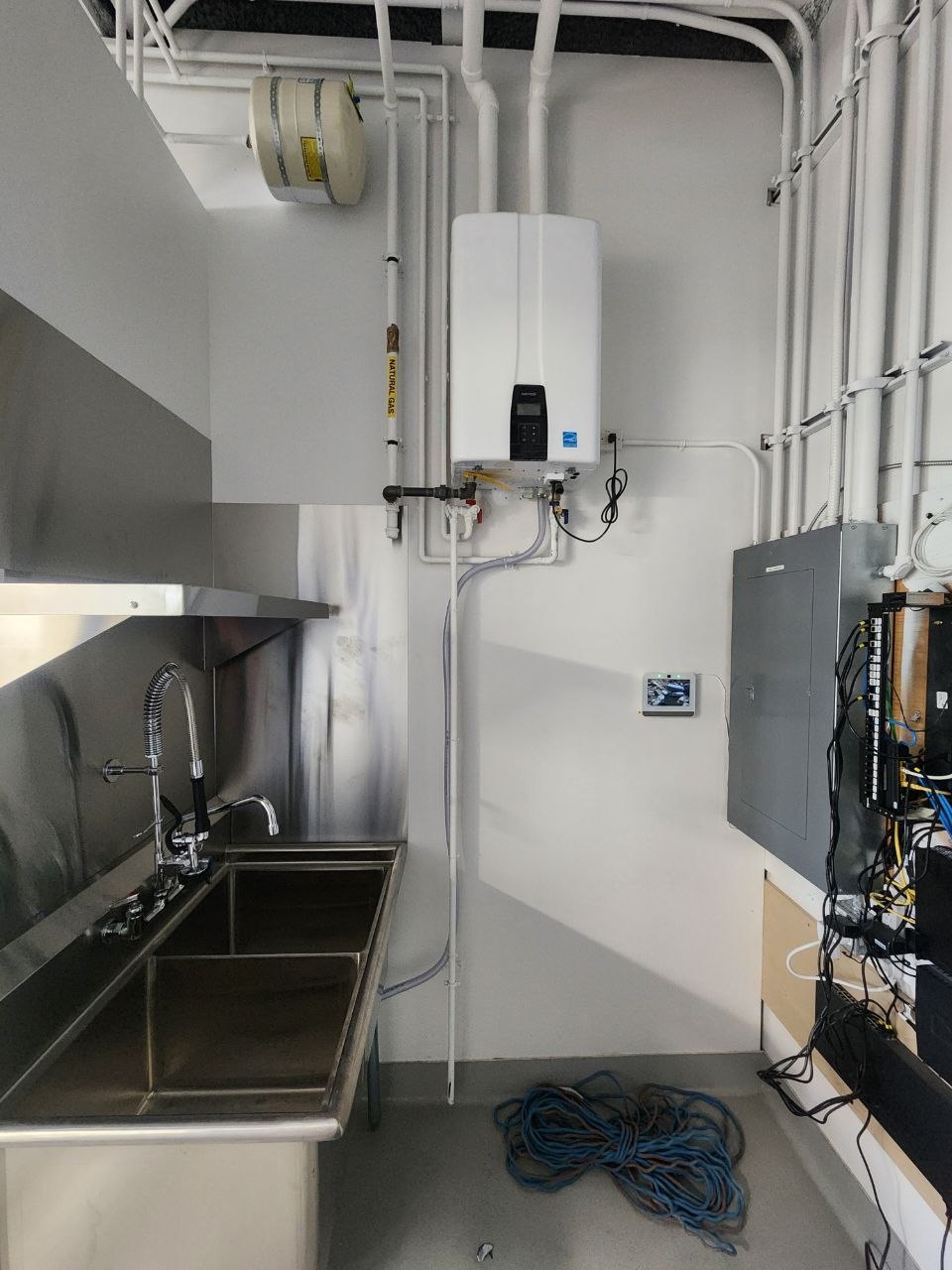 Commercial bakery tankless hot water system beside a three-compartment sink